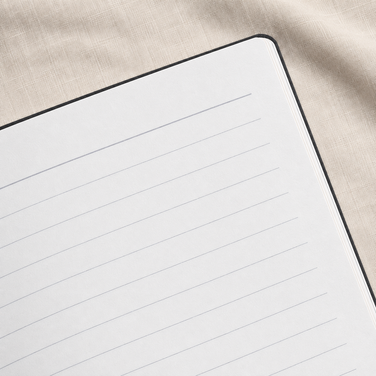 A close-up of a lined notebook page with a black cover, placed on a textured beige fabric background.