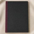 A black hardcover notebook with a linen burgundy spine, placed on a beige fabric background. The brand name 'INFORGE' is embossed on the bottom right corner of the cover.